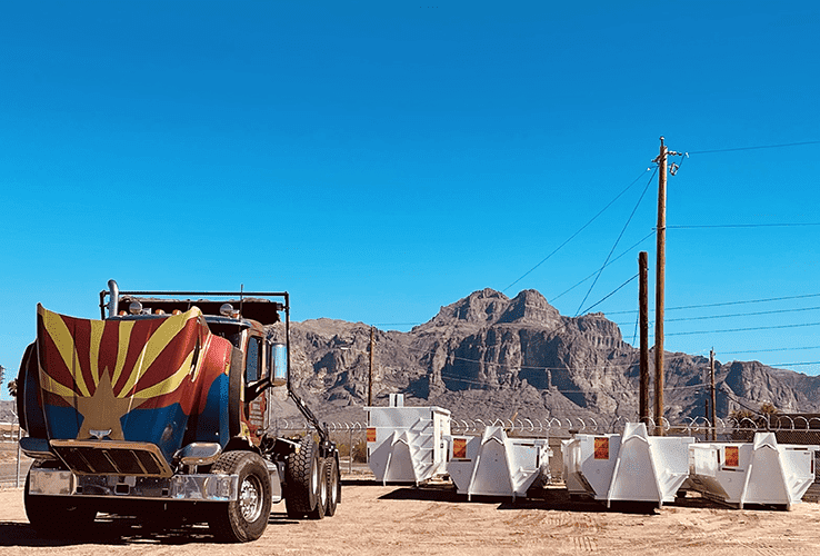 Colorful cement truck beside white barricades in a desert with rocky mountains and blue sky