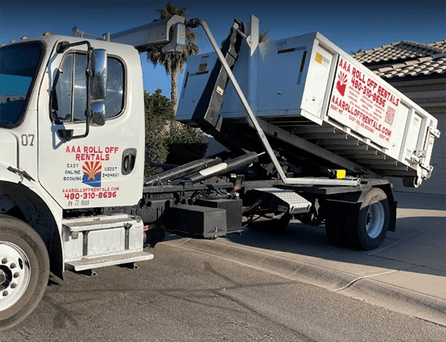 White dump truck with raised bed tipping debris on a sunny street near palm trees