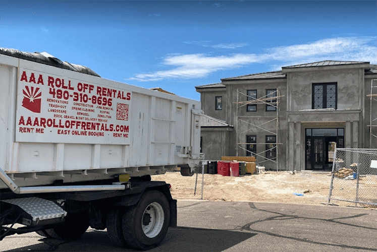 Roll-off dumpster truck beside a construction site with an unfinished building and debris bags