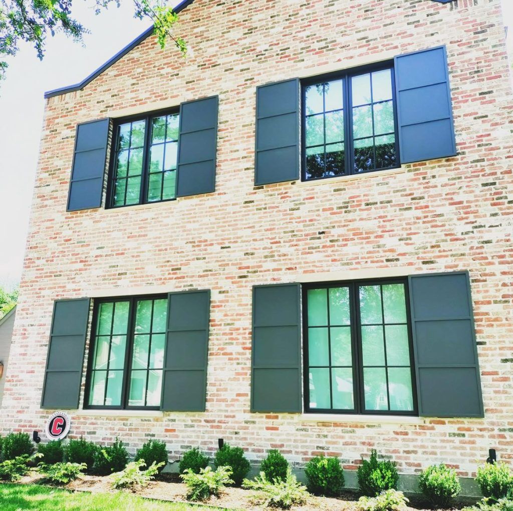 Brick house with black windows and shutters, green landscaping.