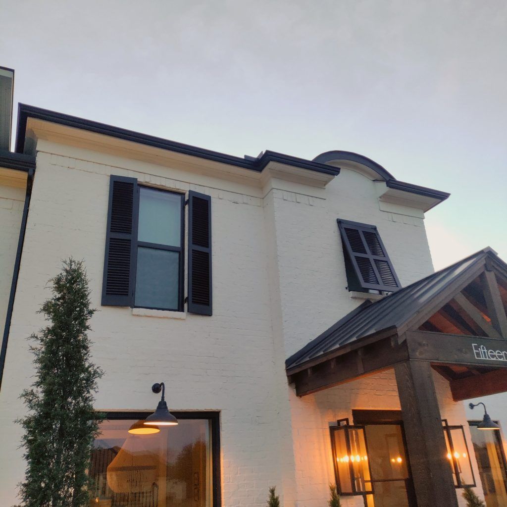 White brick house with black shutters and trim, illuminated at dusk.