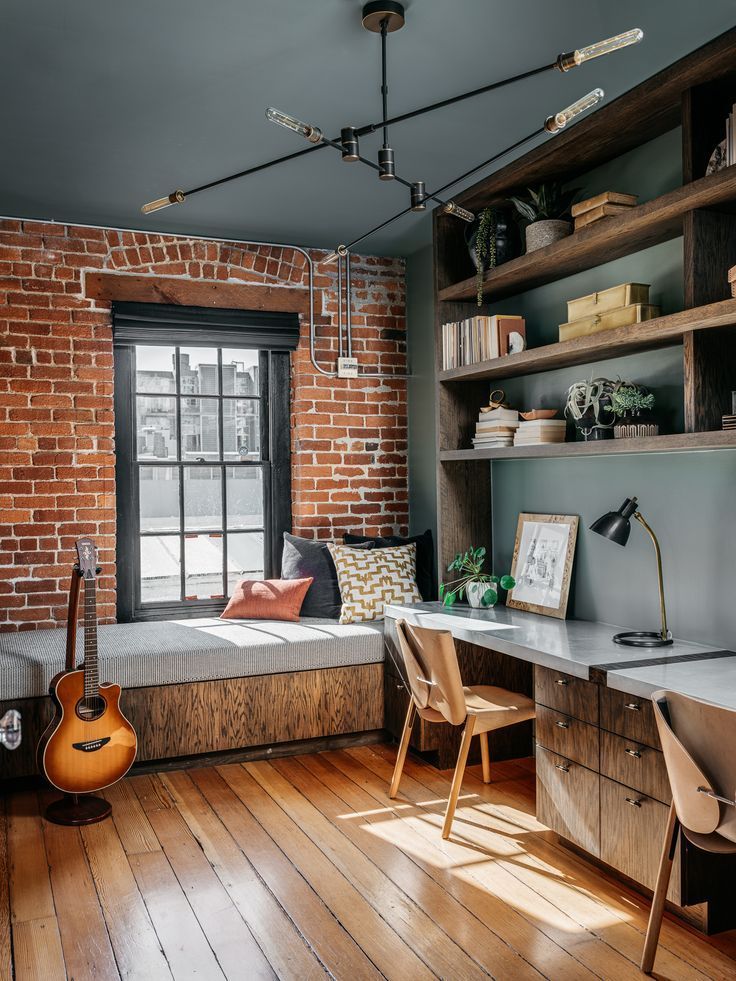 A room with a brick wall , wooden floors , a desk and a guitar.