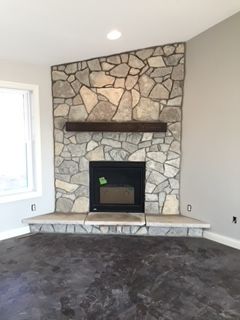A living room with a stone fireplace and a window.