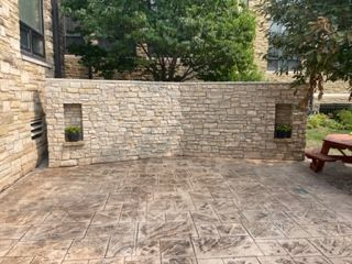 Stone patio with a low stone wall, two small windows, and a red bench under trees