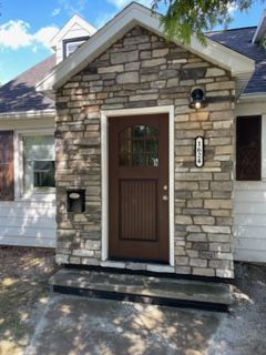Stone-front entryway with brown door, black lantern, and white trim on a house exterior