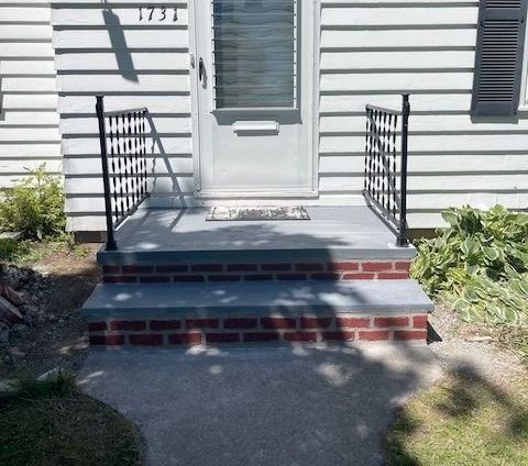 Front porch with blue-gray steps, black railings, and a white door on a house exterior