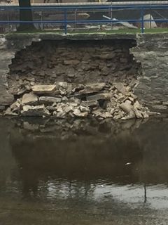 Collapsed stone riverbank wall with exposed rocks above calm water