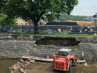 A tractor is working on a stone wall next to a river.