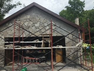 Stone-front house under construction with scaffolding across the front entrance