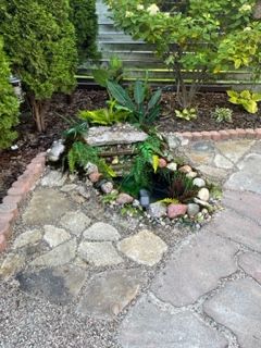 Small stone-bordered garden pond with rocks and green plants beside a paved patio