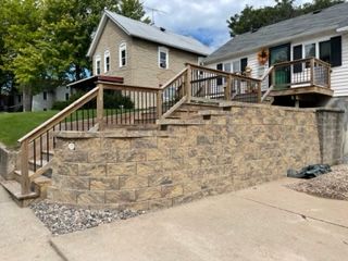 Stone retaining wall and wooden stairs leading to a house entrance on a sloped residential street