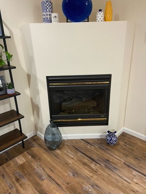 Corner fireplace with beige surround, wood floor, and decorative vases in a living room.