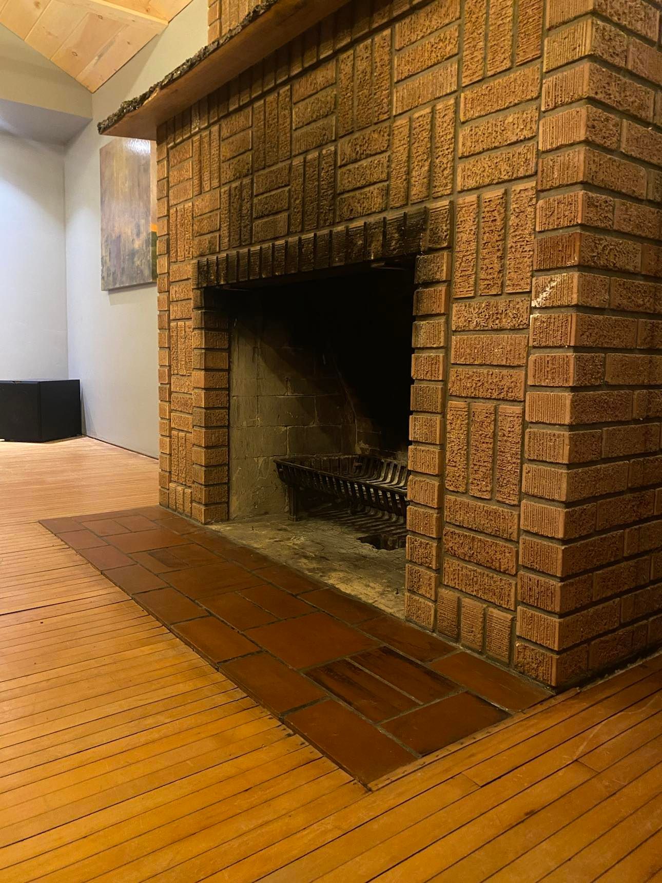 Brick fireplace with dark firebox in a room with a wood floor and staircase nearby