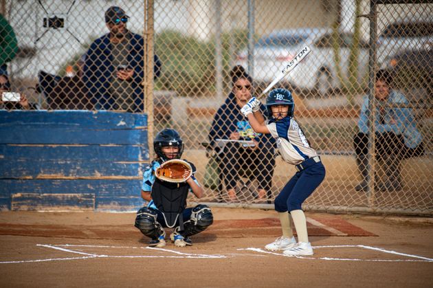 Baseball player sliding into home plate, catcher in front. Blue and gold uniforms, action shot.