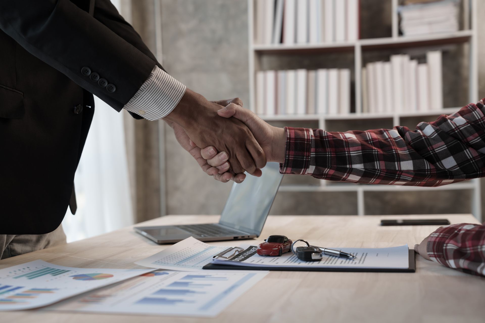 Two people shaking hands over a desk with car keys and documents. Two people shaking hands over a desk with car keys and documents.