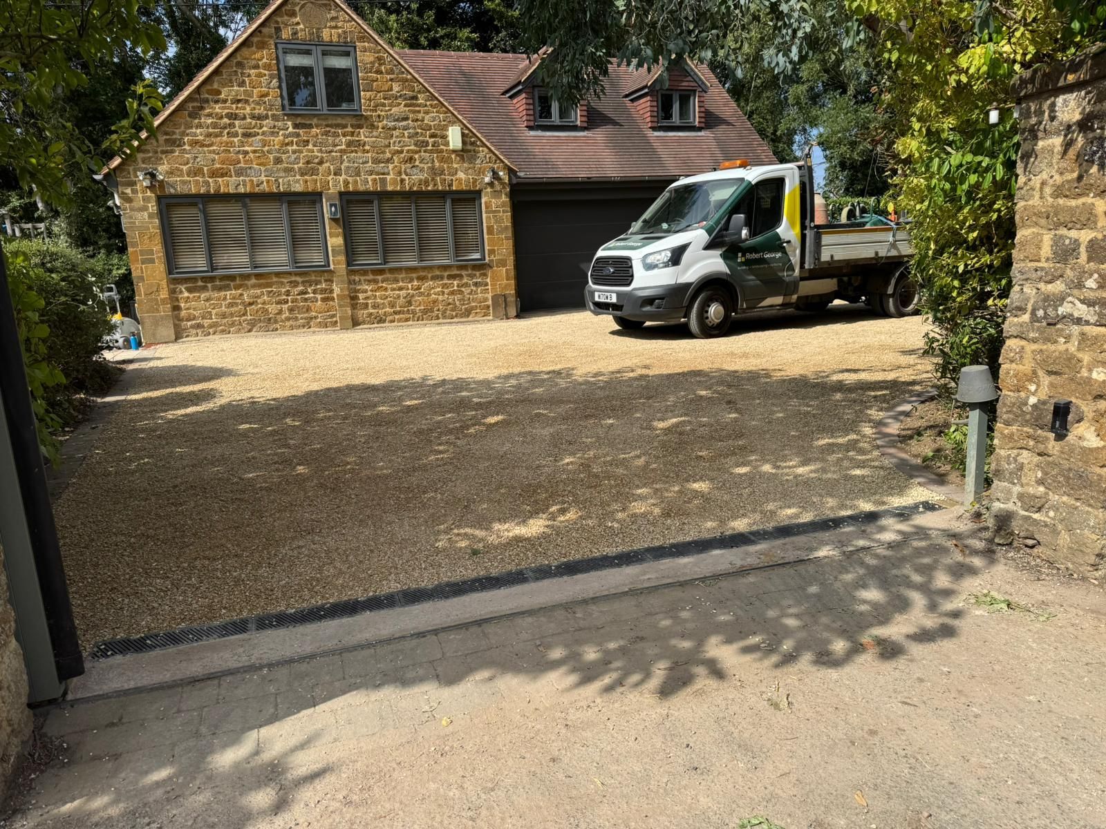 A gravel driveway with a beige stone building and a service truck.