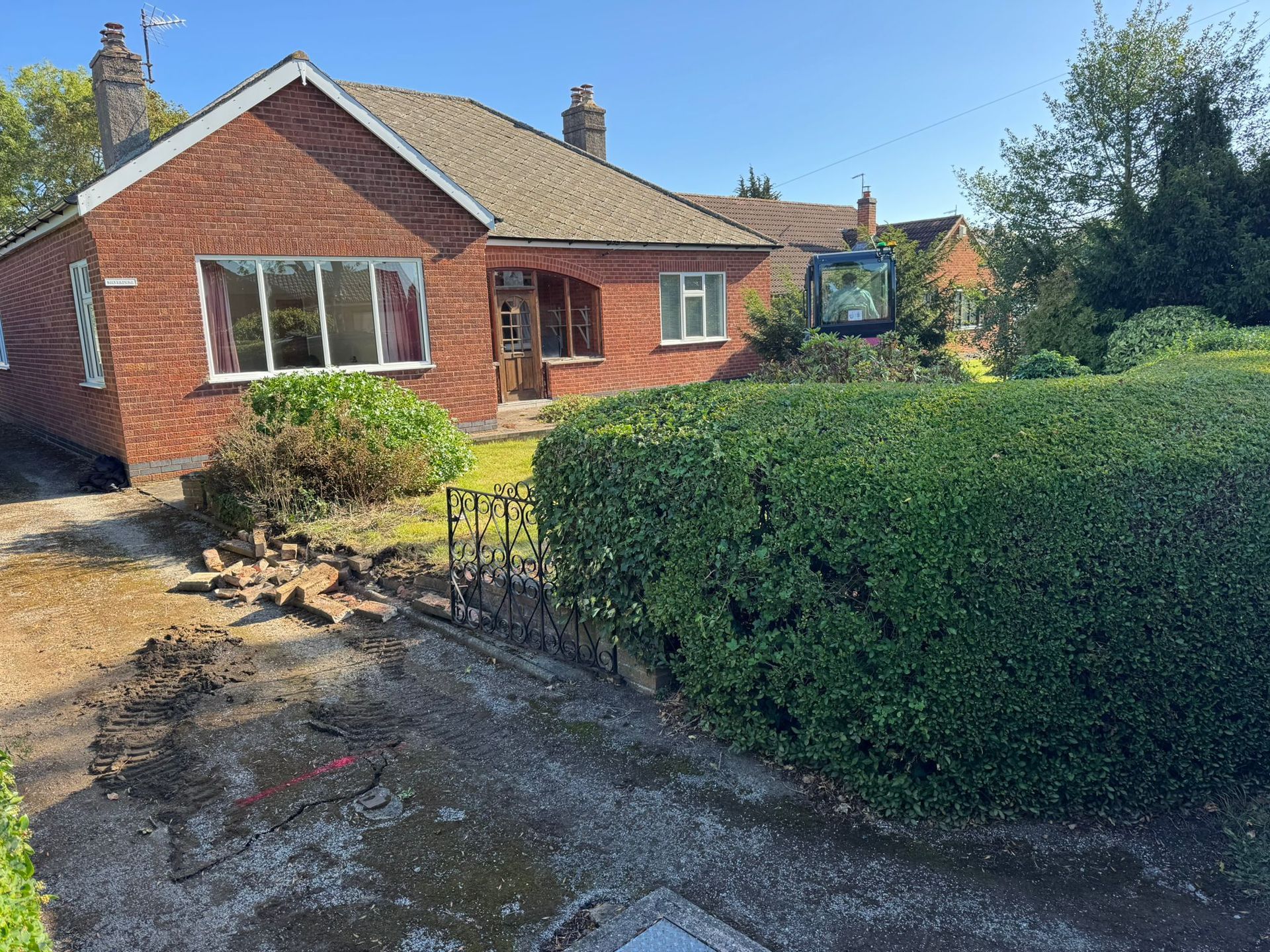 Brick bungalow with a small garden, a clipped hedge, and a dark paved driveway.