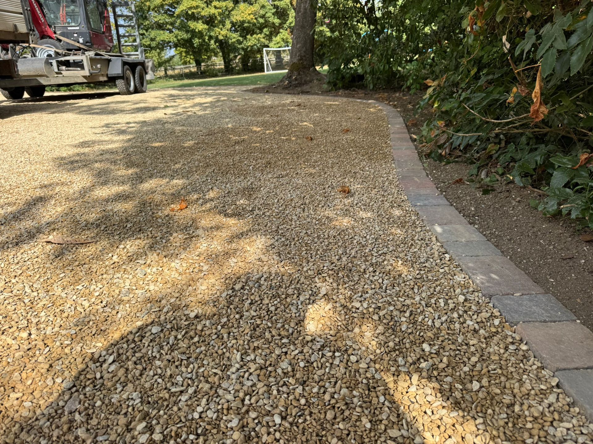 Gravel driveway with a brick border, tree and greenery in the background, a truck in the distance.