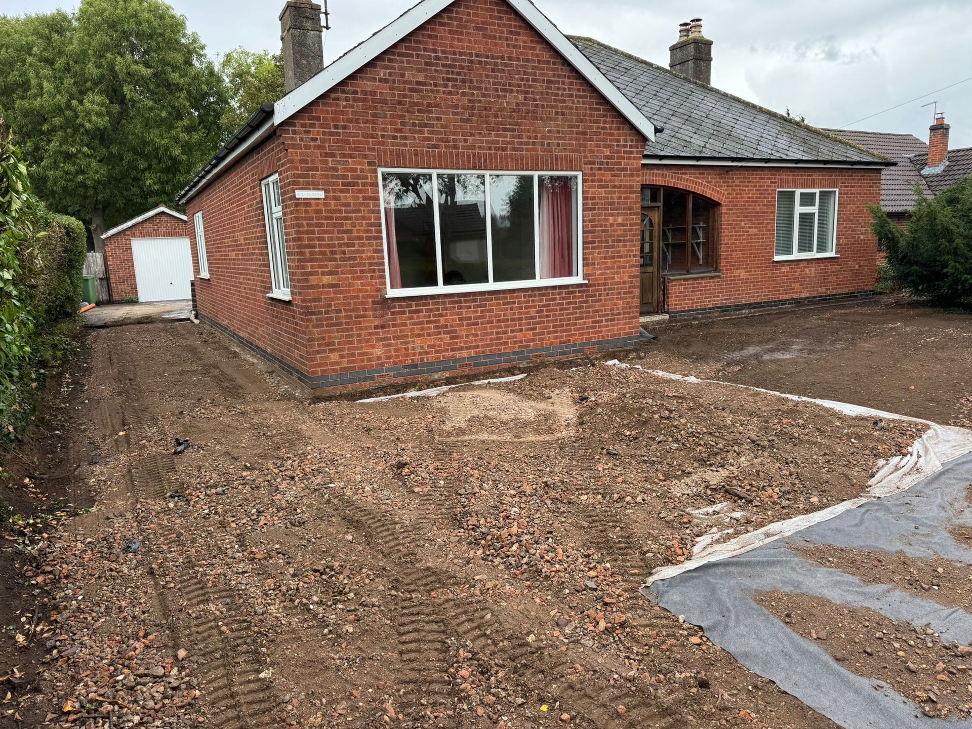Red brick bungalow with a gravel driveway under construction.