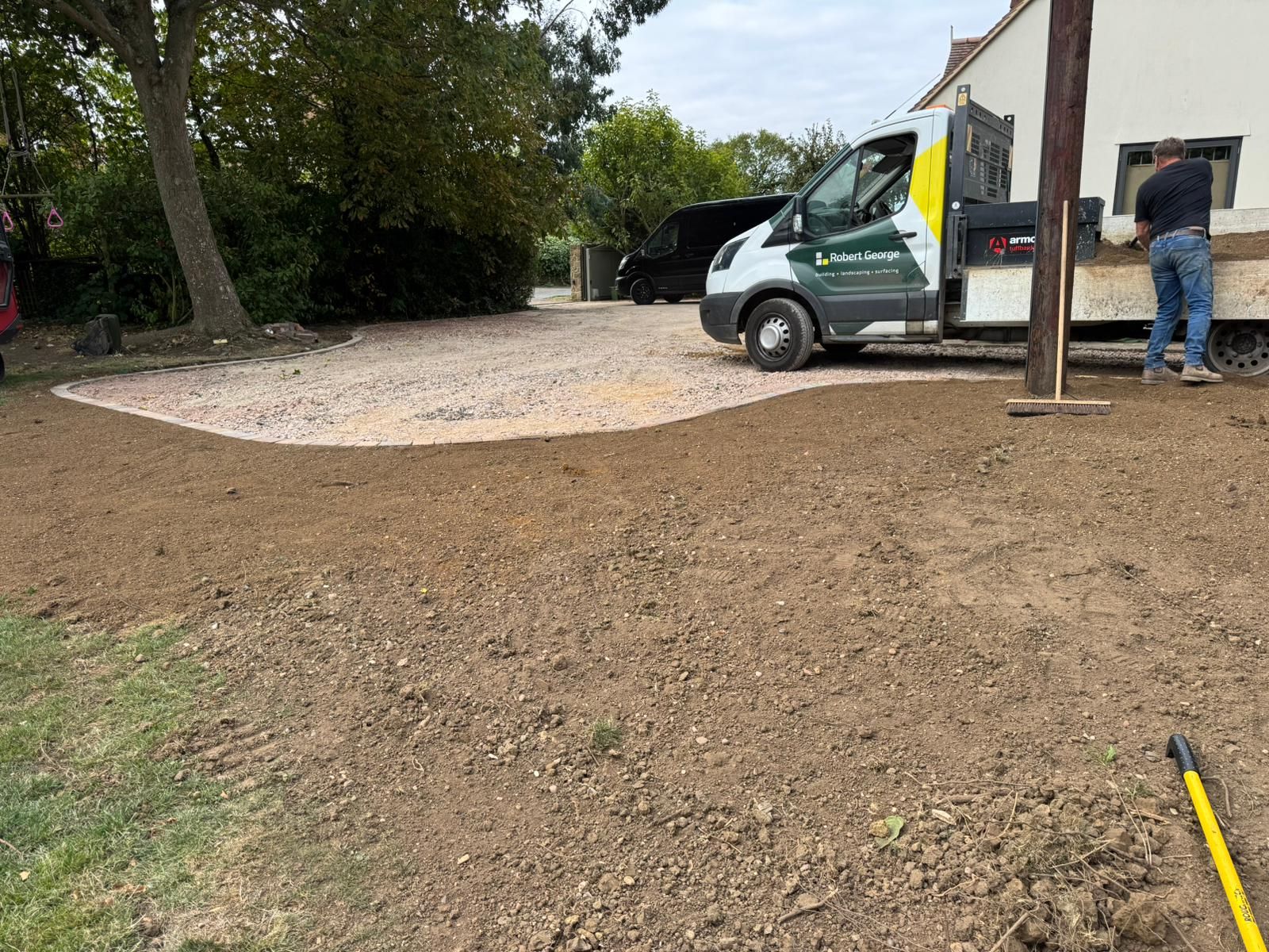 Gravel being laid for a new driveway. A person stands near a white van parked by a house.