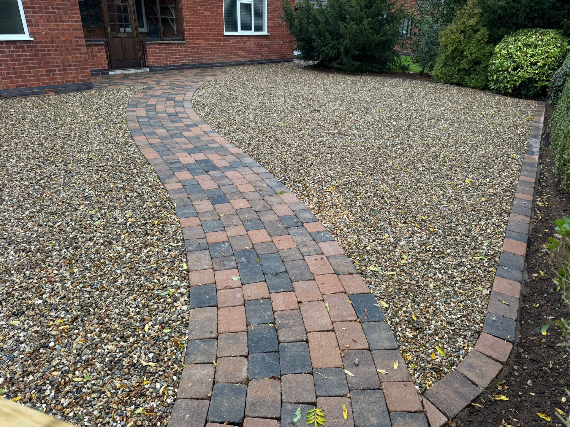 Brick pathway through gravel driveway to a brick home.