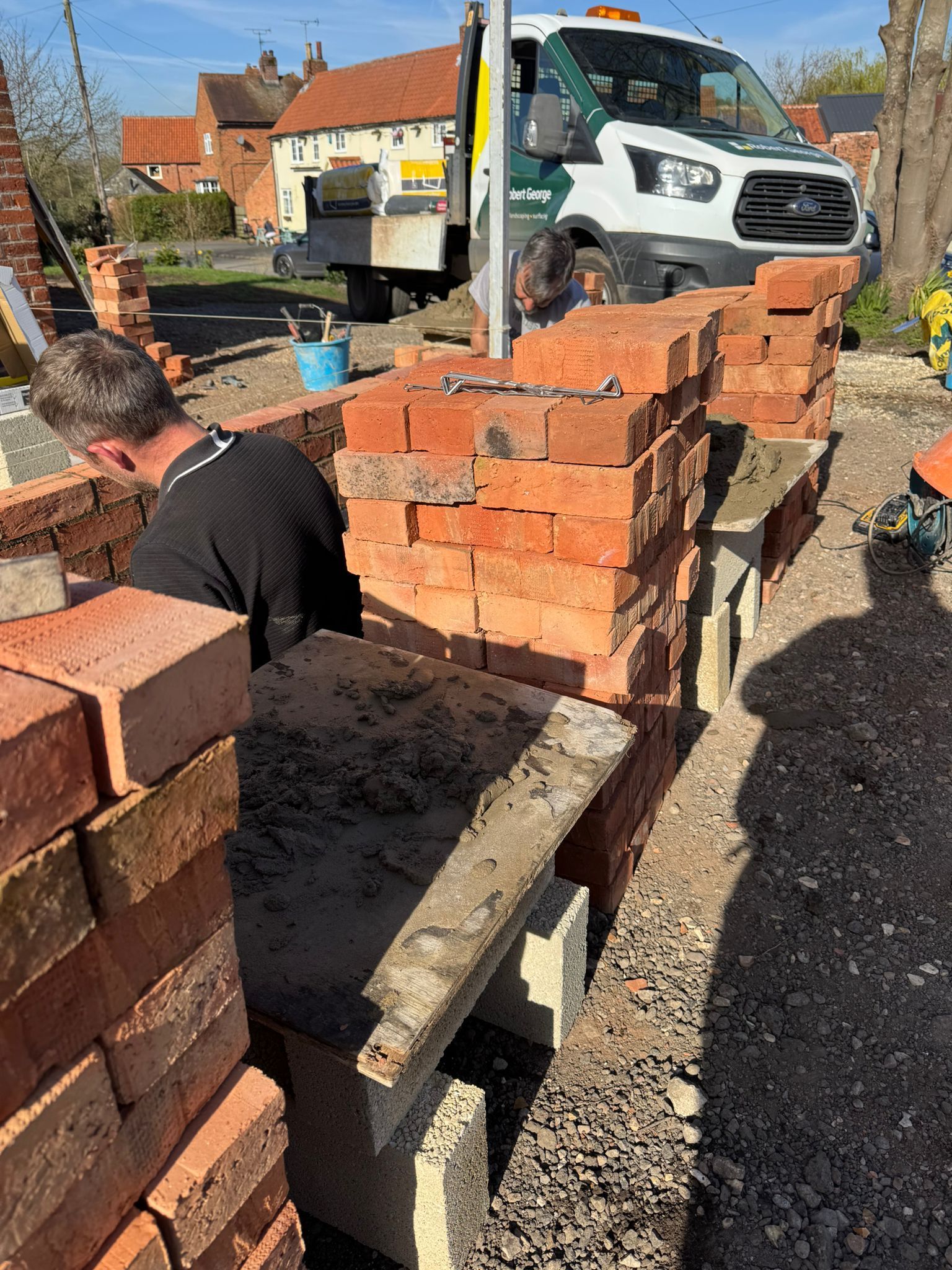 A bricklayer constructing a brick wall outdoors next to a work van.