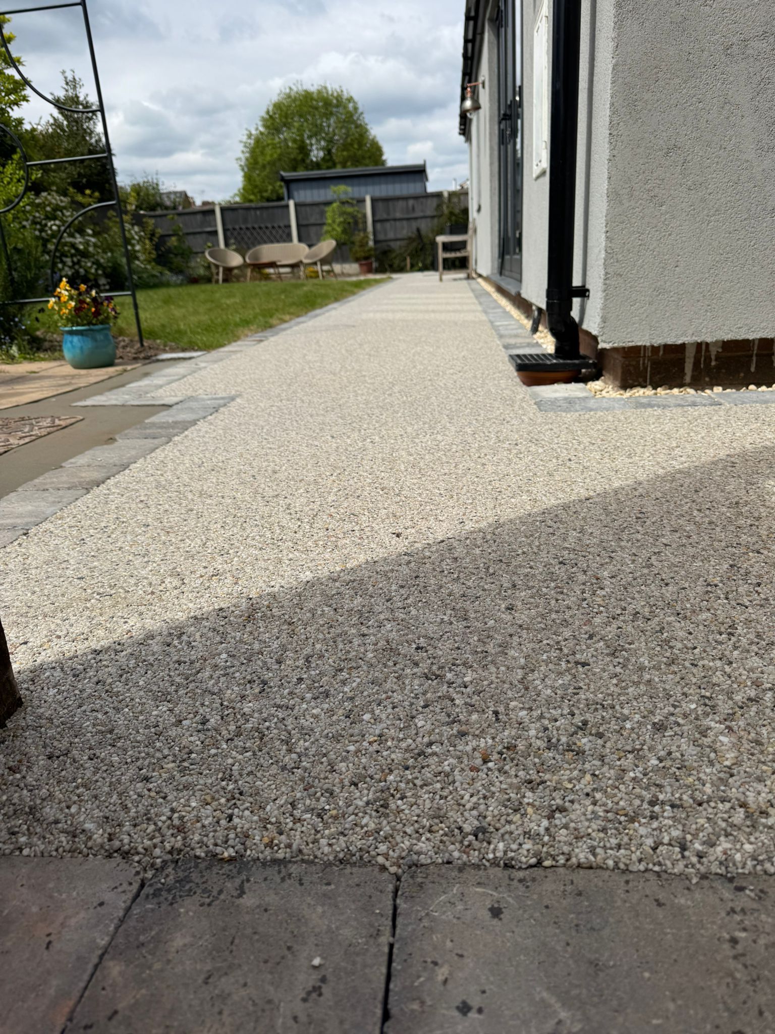 Gravel pathway in a backyard, bordered by paving stones and the side of a house.