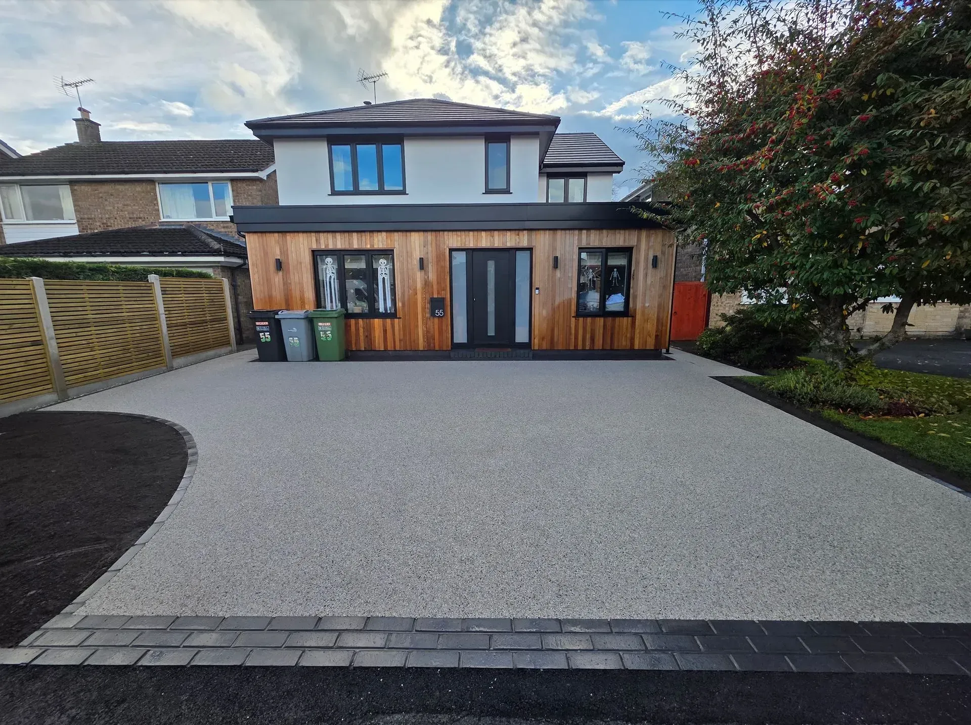 House with gravel driveway, wood-paneled extension, and blue sky.