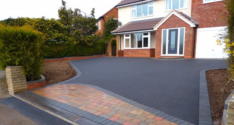 Driveway leading to a two-story brick and white house, with a black asphalt surface.