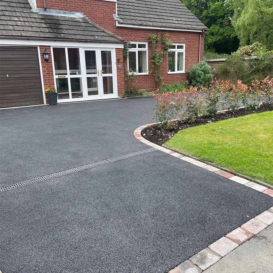 Driveway leading to a brick house with white double doors, a brown garage door, and a landscaped border.