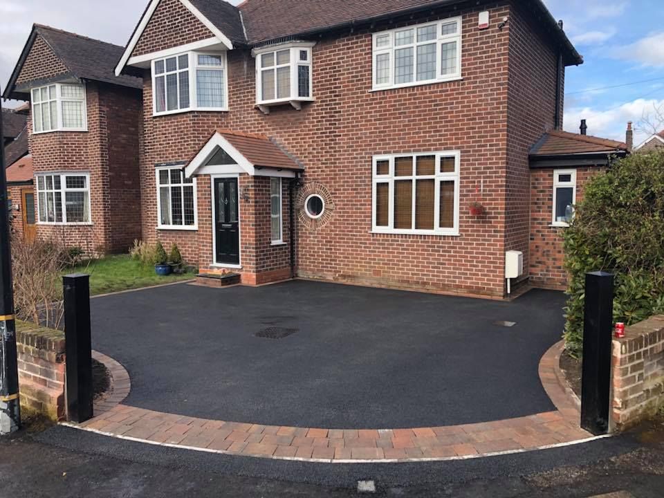 Brick house with asphalt driveway, bordered by red brick, and black posts.