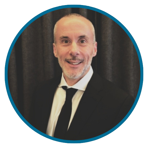 A man in a black suit and tie smiles, inside a teal circle.