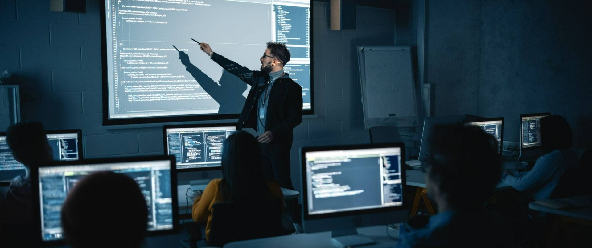 A man is giving a presentation to a group of people in front of a projector screen.