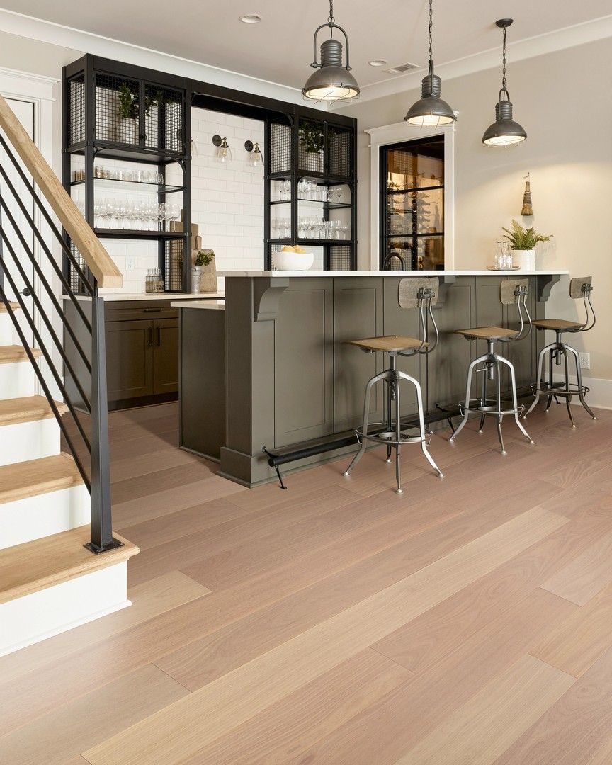 Modern kitchen with island bar stools, black-framed shelving, pendant lights, and a staircase.
