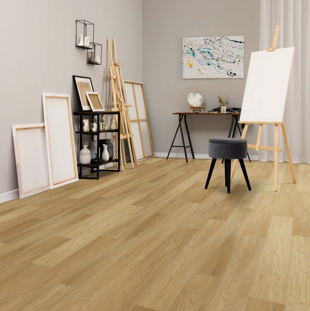 Bright art studio with easels, framed canvases, shelves, desk, and light wood floor.