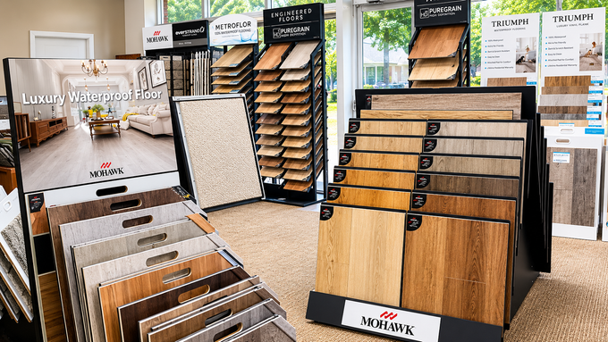 Display of flooring samples in a showroom, with wood and tile boards on racks and signs in the background