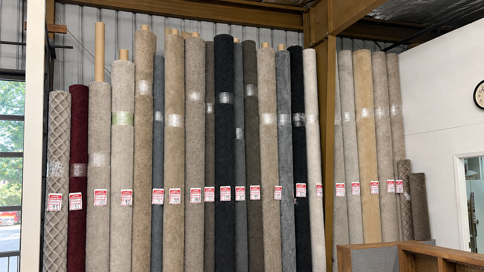 Carpet rolls standing upright in a showroom, with various gray, beige, black, and red samples.