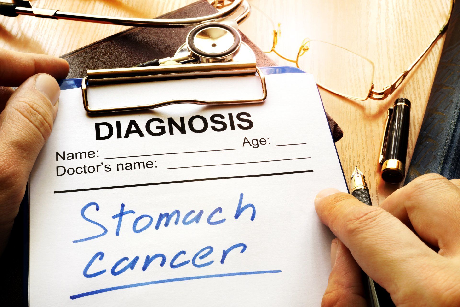 A clipboard on a table with a diagnosis form stating Stomach Cancer on it.
