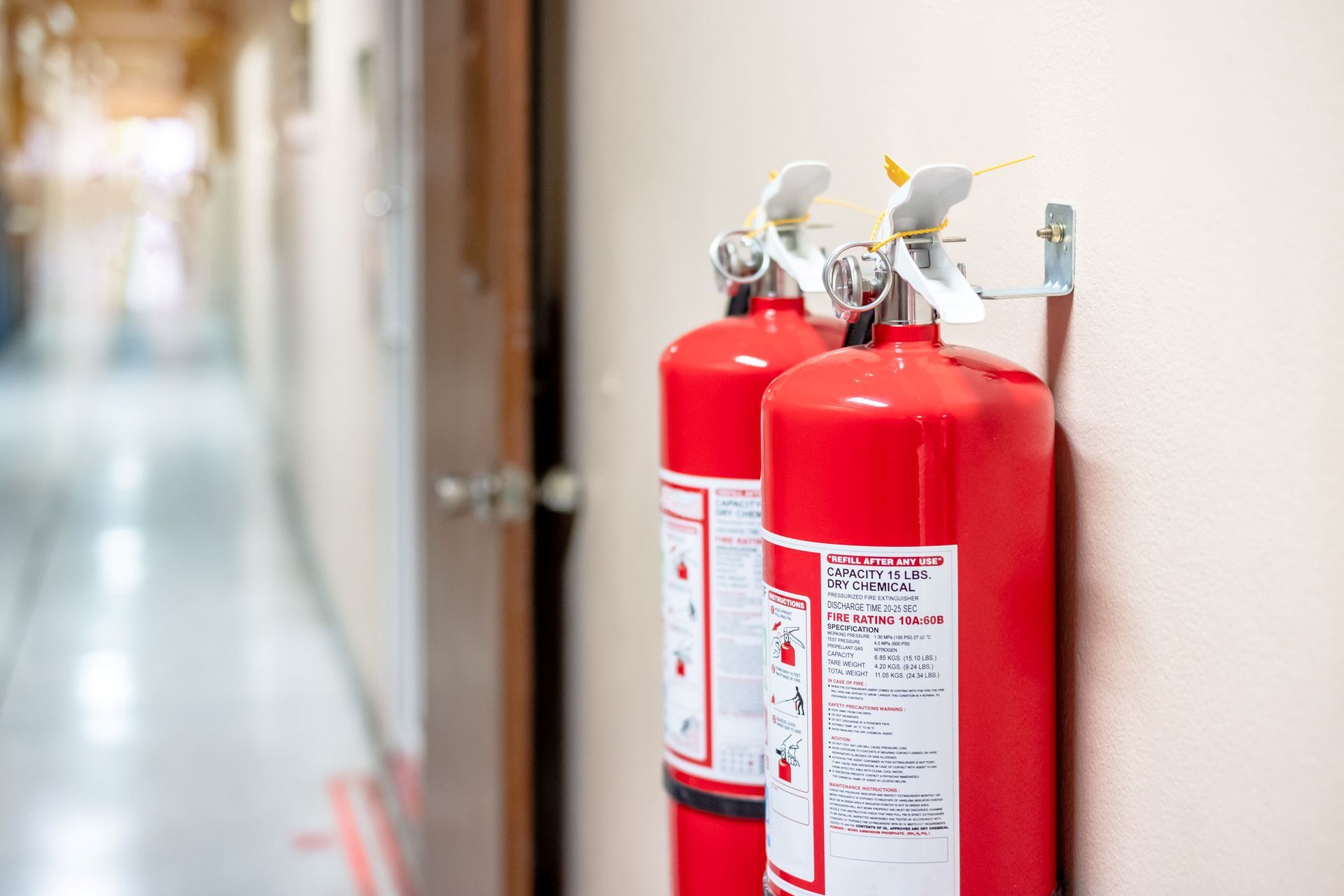 Two red fire extinguishers mounted on a wall in a hallway Two red fire extinguishers mounted on a wall in a hallway