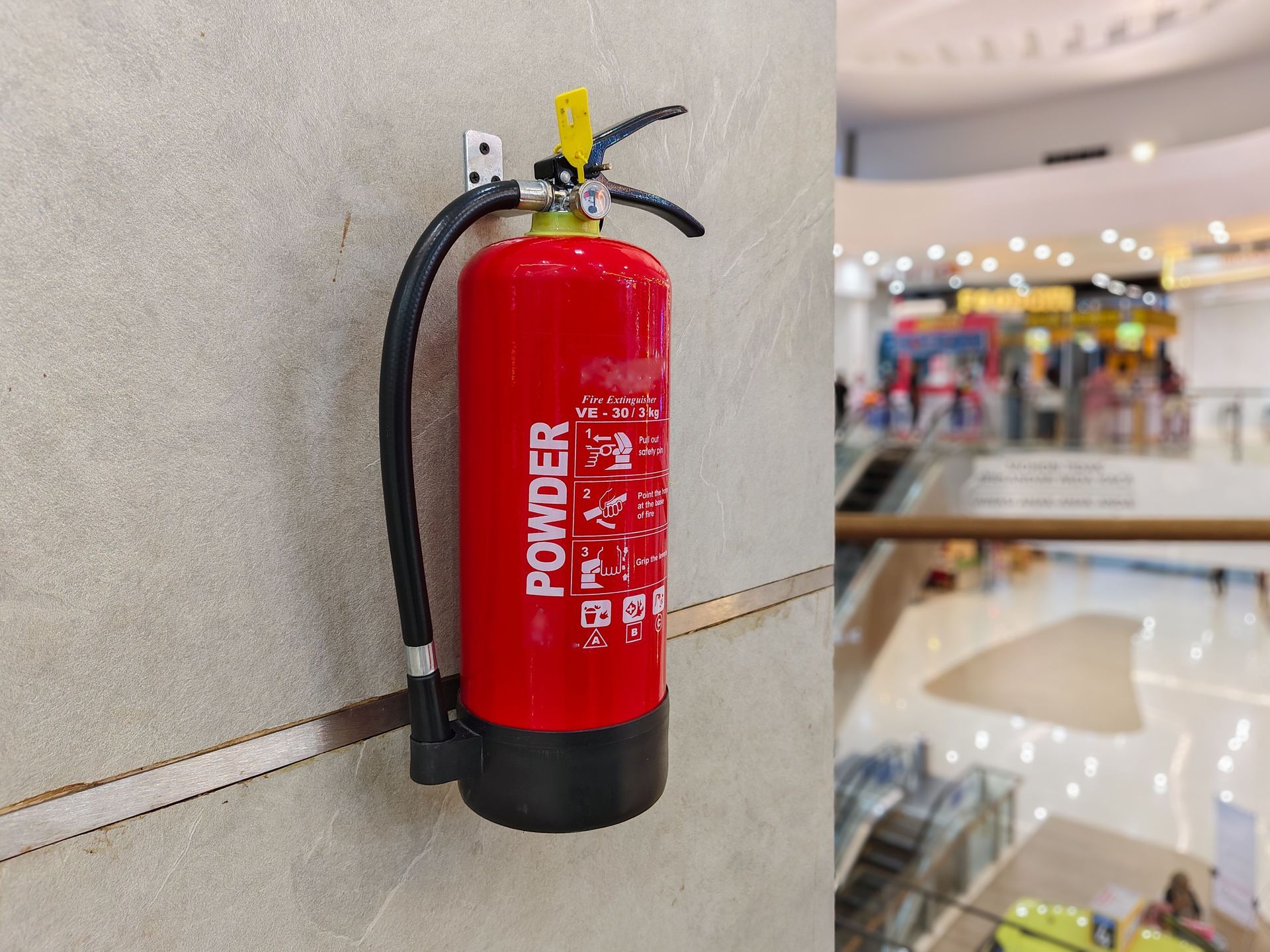Red fire extinguisher mounted on a wall in a mall hallway.