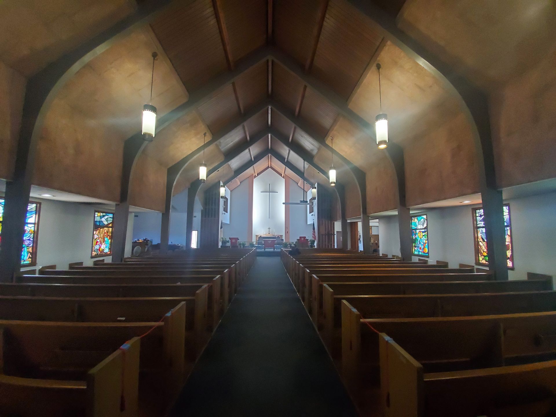 Empty church interior with wooden pews, vaulted ceiling, and stained-glass windows leading to a bright altar