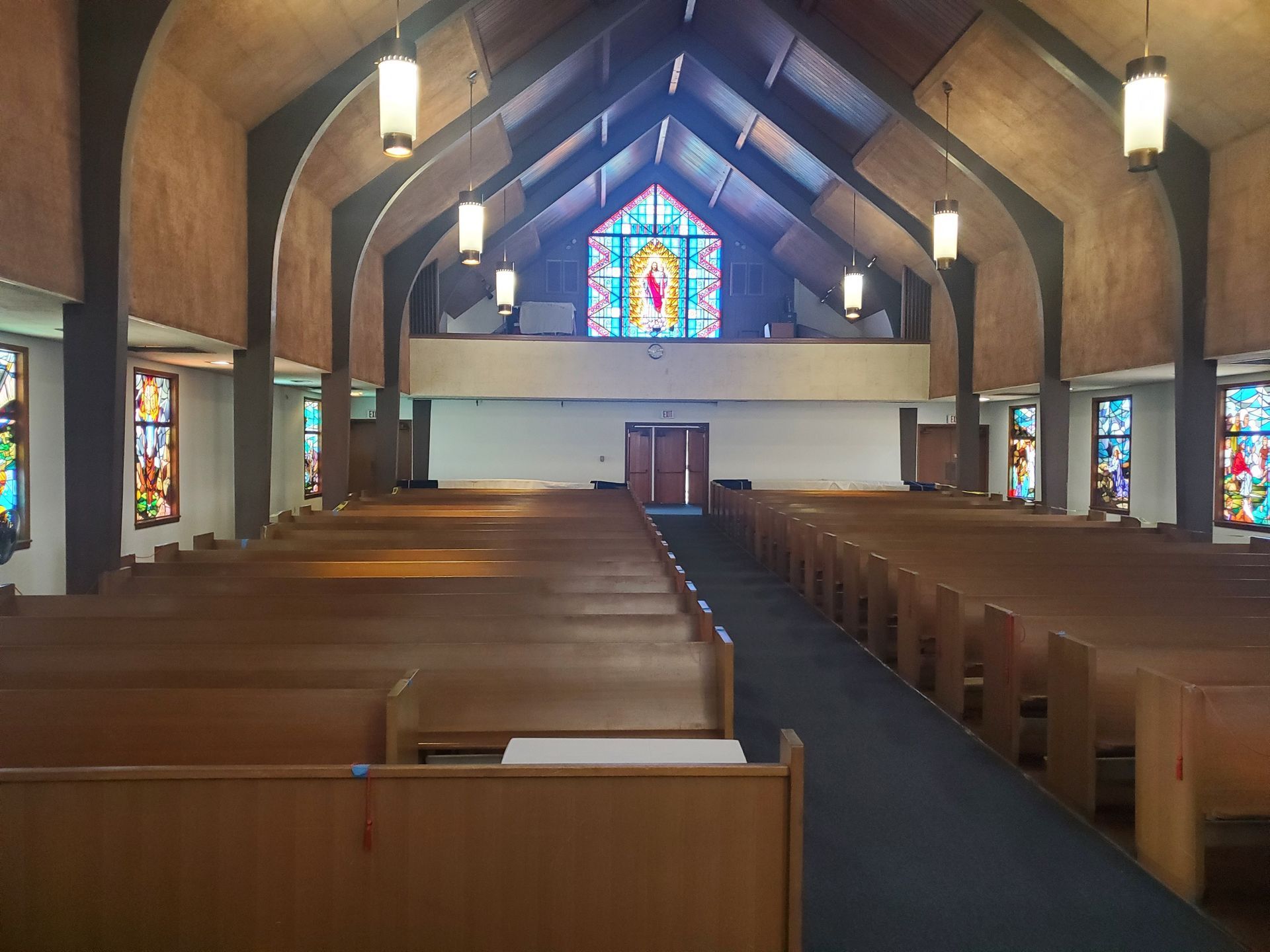 Empty church interior with wooden pews, vaulted ceiling, and stained-glass windows at the front.