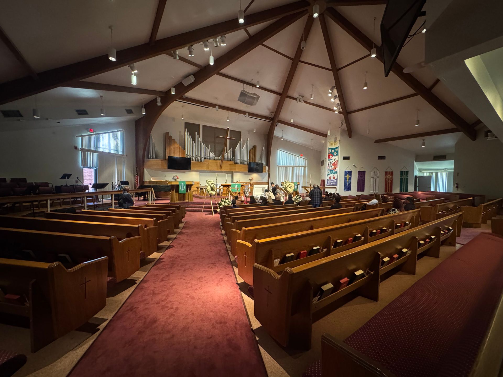 Empty church sanctuary with wooden pews, red carpet aisle, and altar under a high beamed ceiling