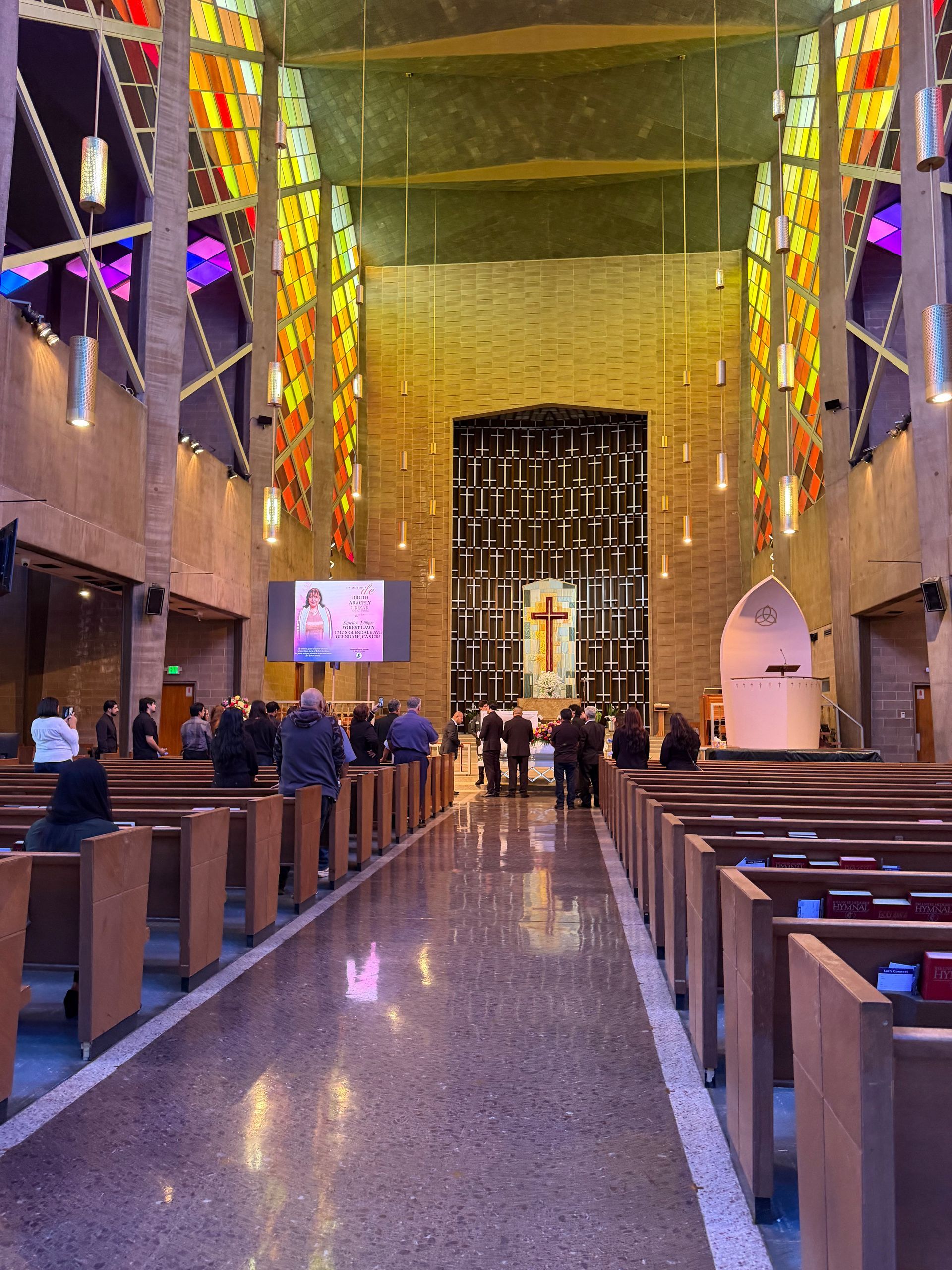 Church interior with colorful stained glass, pews, and people gathered near the altar