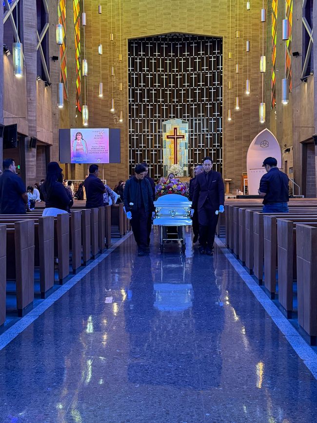 Church interior with blue-lit aisle, people seated in pews, and a glowing cross at the altar.