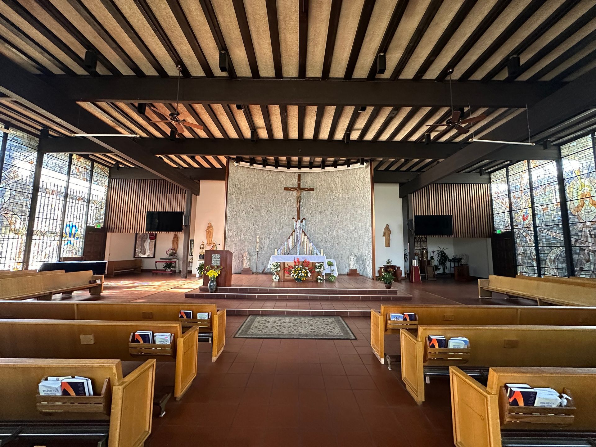 Church interior with wooden pews, central altar, and crucifix under a dark beamed ceiling.