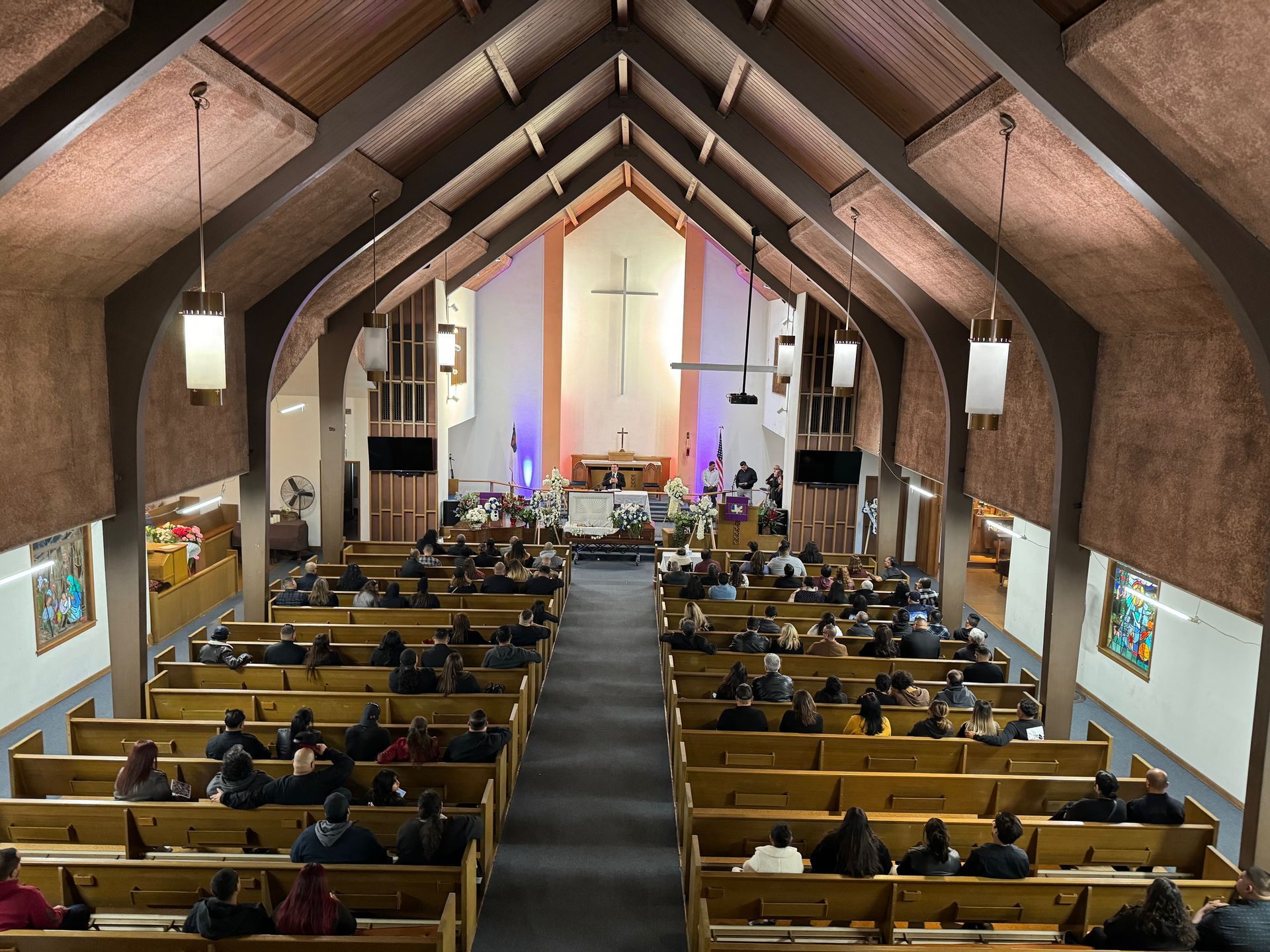 Church sanctuary with congregants seated in pews facing the altar and cross at the front