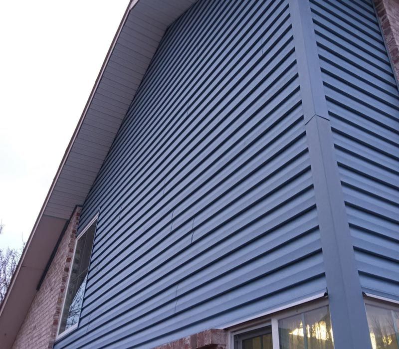 Blue-gray siding on a house exterior with a steep roof overhang and window lights visible below
