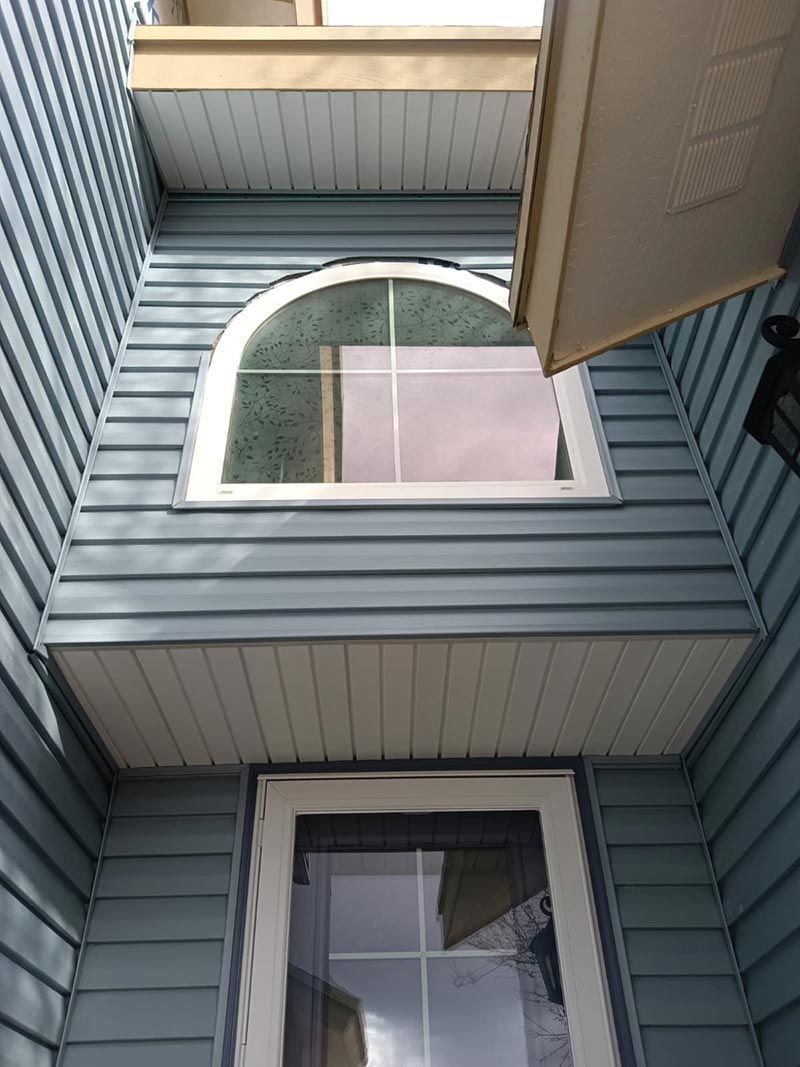 Upward view of blue-sided house with windows and an open awning above.
