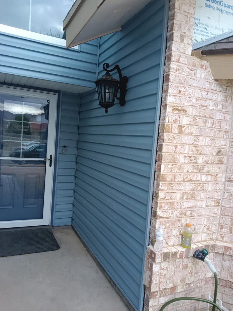 Covered apartment entrance with blue siding, glass door, wall lantern, and brick column.